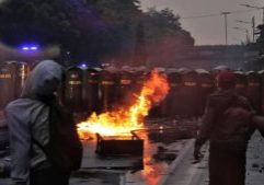 Api menyala di depan barikade keamanan di Pejempongan.Massa dan aparat saling balas lemparan dalam bentrok ini.Aparat menembakkan gas airt mata ke arah masdsa, dibalas dengan lemparfan batu hingga petasan.